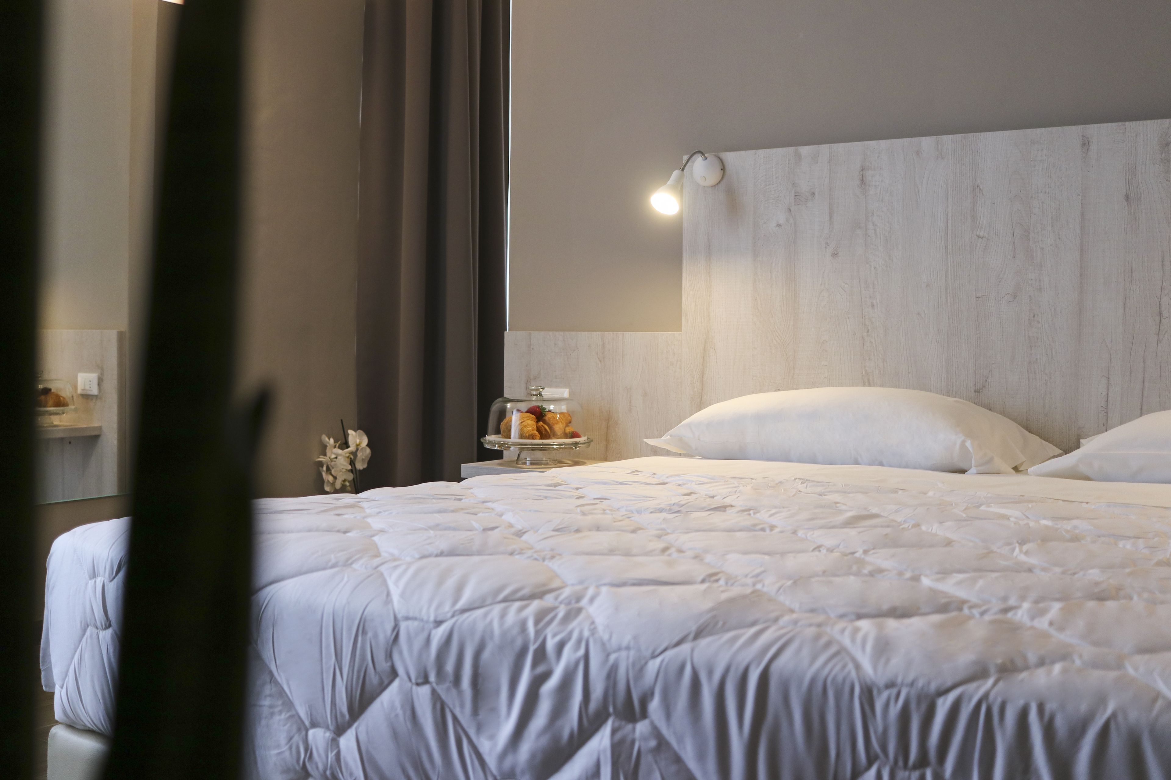 A neatly made bed with white bedding, a bedside table with a lamp, and a mirror on the wall.