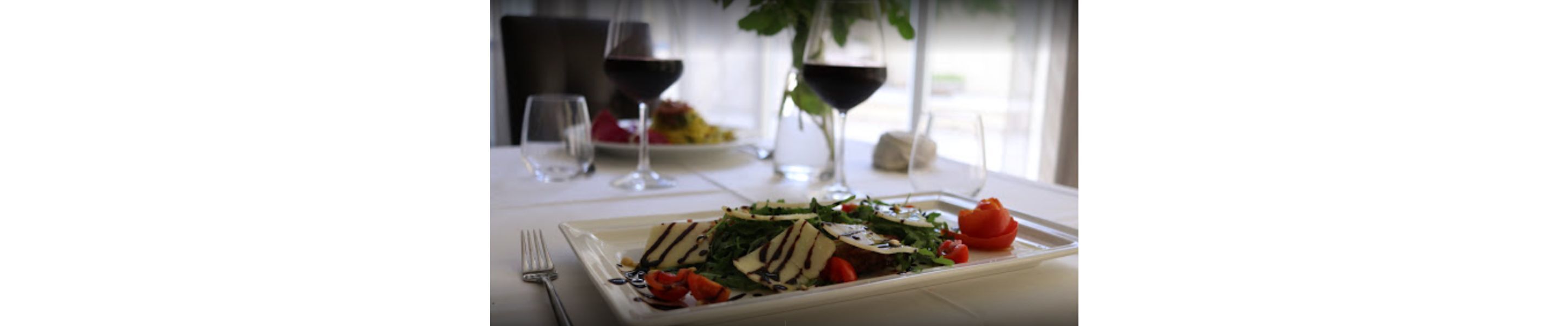 A dining table with a plate of food, a wine glass, and a fork.