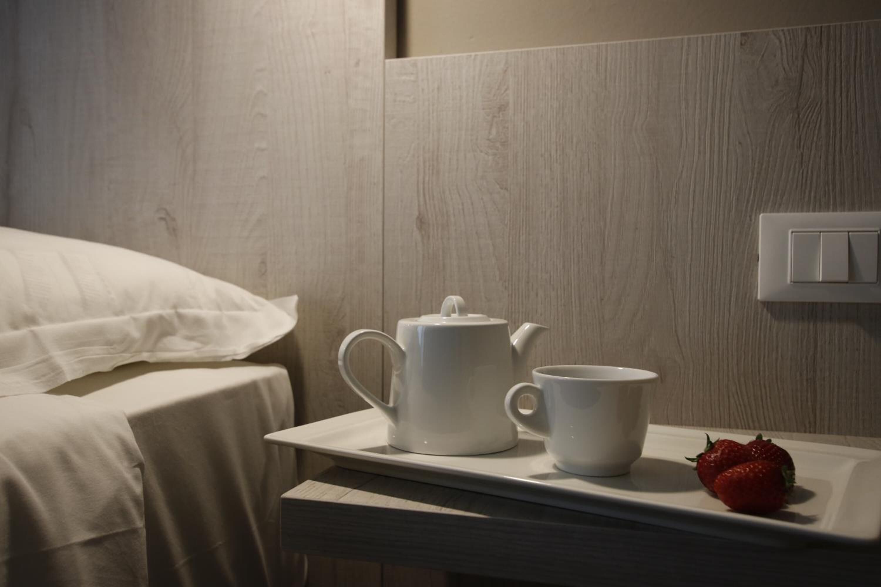 A neatly made bed with white linens, a white tray with a teapot and cup, and a strawberry on the tray.