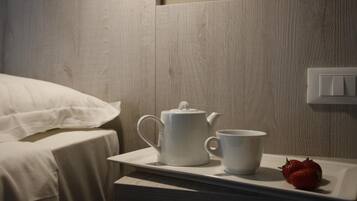 A neatly made bed with white linens, a white tray with a teapot and cup, and a strawberry on the tray.