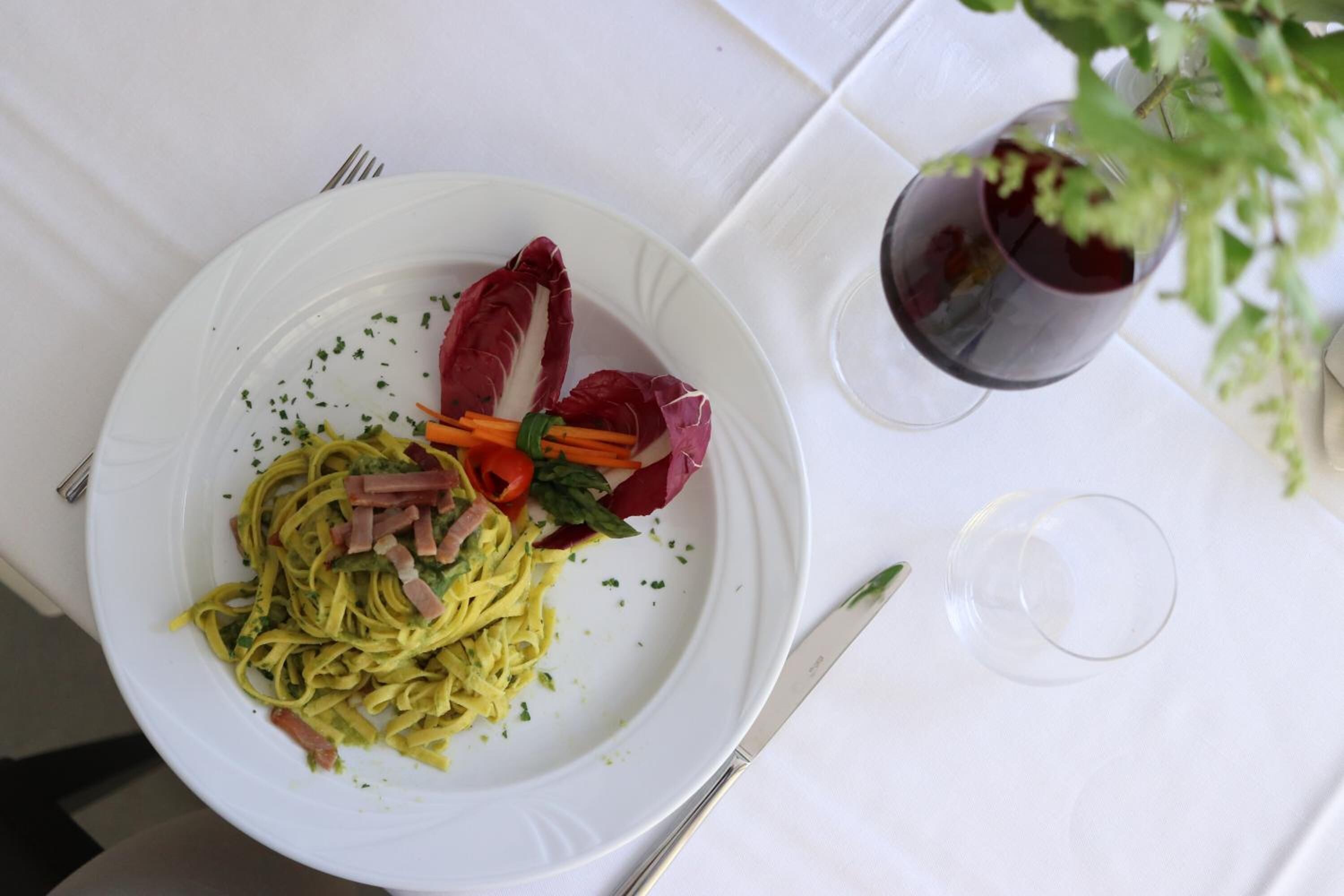 A white plate with pasta, vegetables, and a red garnish on a white tablecloth.