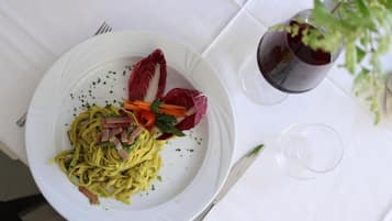 A white plate with pasta, vegetables, and a red garnish on a white tablecloth.