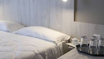 A neatly made bed with white linens, a bedside table with a tray holding four clear glasses, and a white wall with a light fixture.