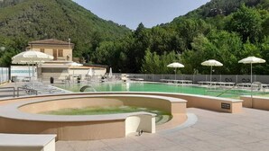 A pool area with a hot tub, lounge chairs, and umbrellas. - Hotel Terme di Frasassi (Genga)
