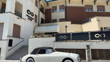 Un coche descapotable blanco antiguo estacionado frente a un hotel con una escalera que lleva a la entrada.