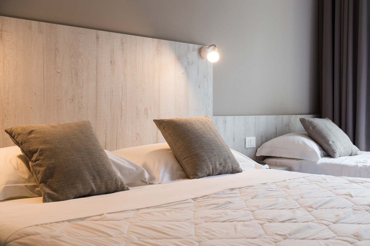 A hotel room with a large bed, two pillows, a headboard, and a wall-mounted light.