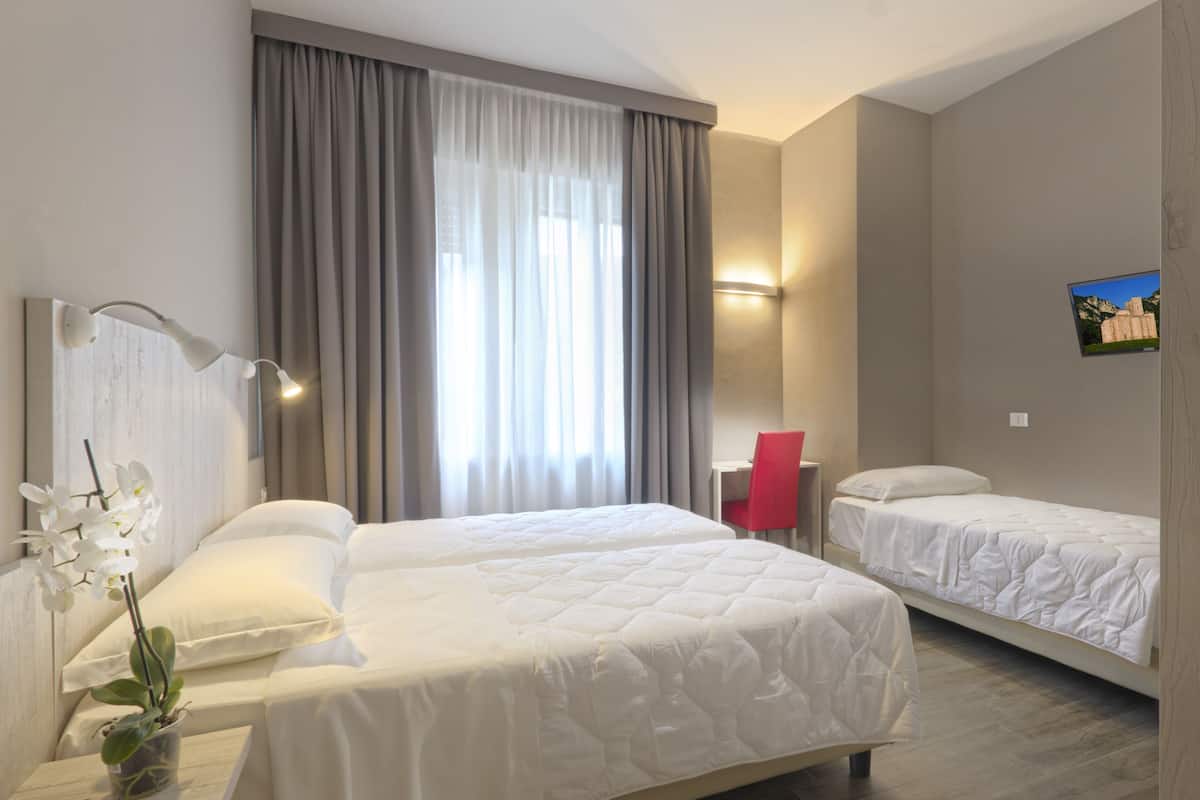A hotel room with two beds, a desk, a chair, a potted orchid, and a painting on the wall.