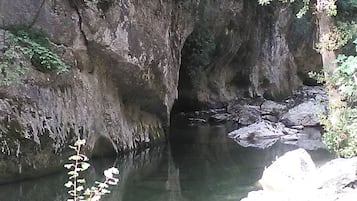 Entrada natural de uma caverna com piscina de águas límpidas na base, rodeada por falésias rochosas e vegetação.