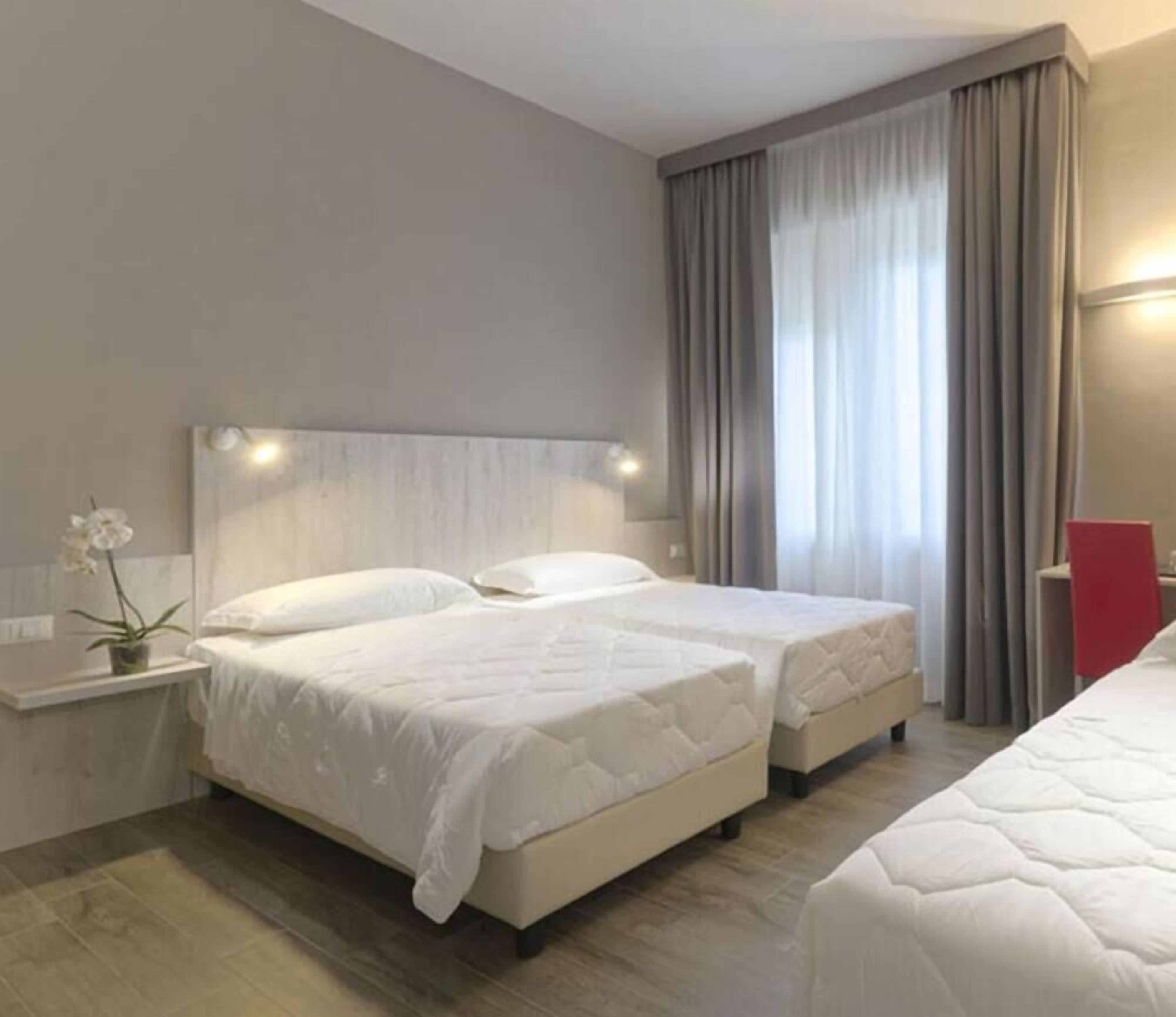 A hotel room with two beds, a nightstand with a plant, and a large window with curtains.