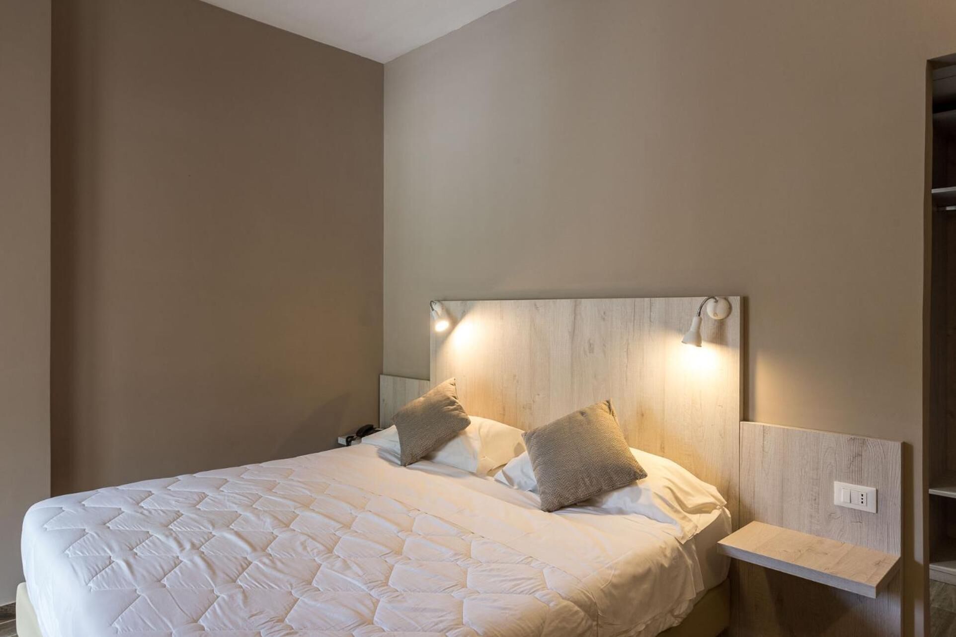 A neatly made bed with a quilted white duvet, two pillows, and a wooden headboard with integrated lighting.