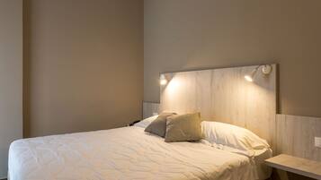 Ein ordentlich bezogenes Bett mit einer gesteppten Decke und zwei Kissen, ein Nachttisch mit einer Lampe und ein Holz-Kopfteil.