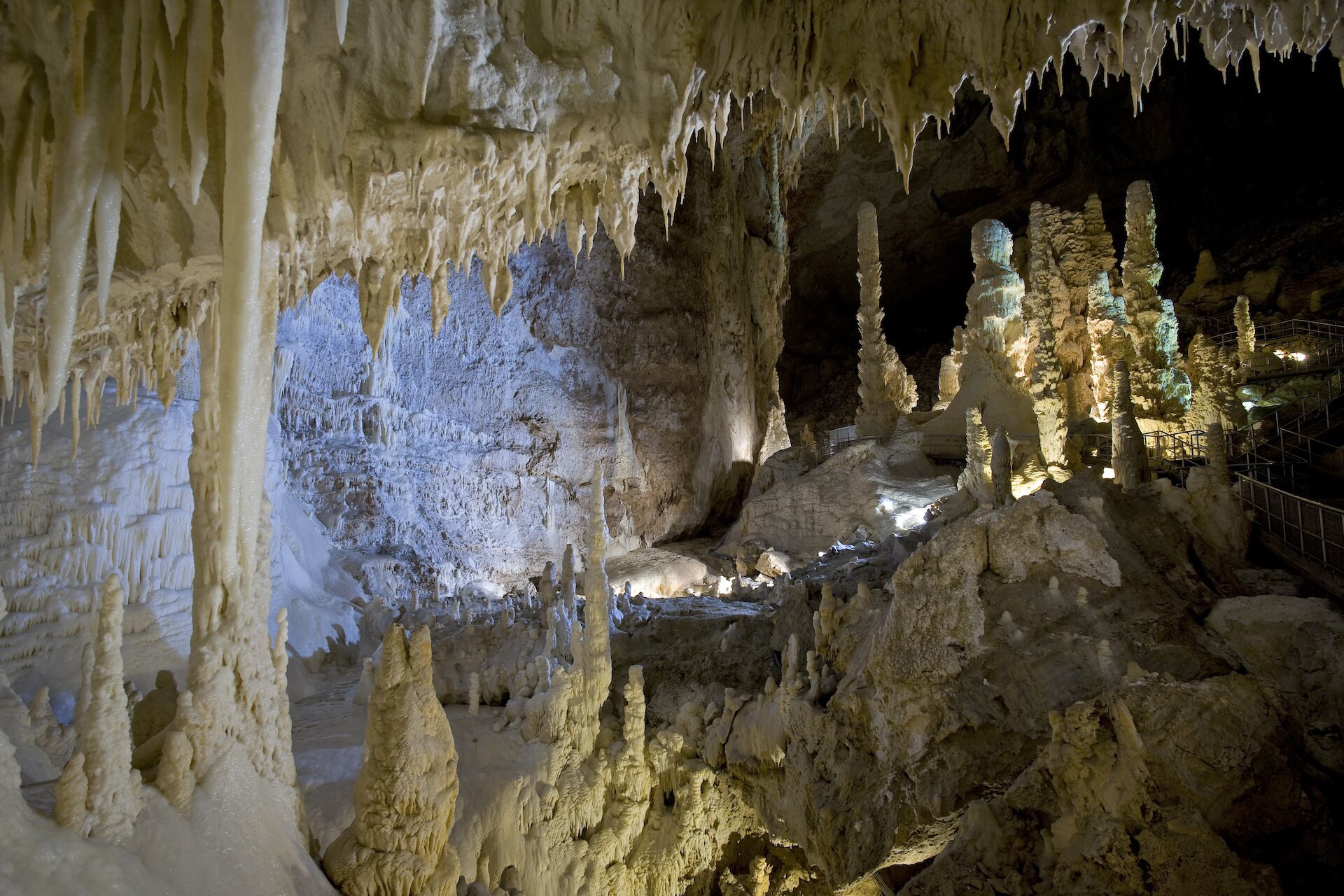 A cave with stalactites and stalagmites, illuminated by artificial lighting.
