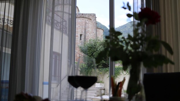A dining table with a wine glass and a vase with a red rose, overlooking a historic stone building and greenery. - Hotel Terme di Frasassi (Genga)