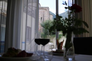 A dining table with a wine glass and a vase with a red rose, overlooking a historic stone building and greenery. - Hotel Terme di Frasassi (Genga)