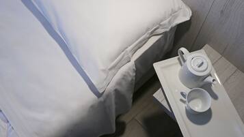 A neatly made bed with white bedding, a white tray with a teapot and cup, and a wooden floor.
