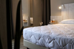 Ett hotellrum med en stor säng, ett nattduksbord med en lampa, en spegel och en liten vas med blommor.