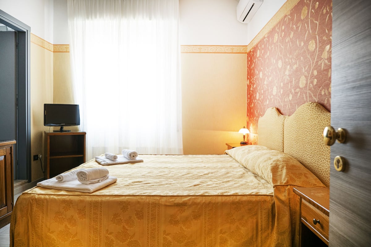 Une chambre d’hôtel comprenant un lit, un téléviseur posé sur un meuble, une table de chevet avec une lampe et une armoire.
