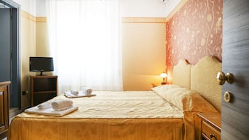 A hotel room with a bed, a television on a stand, a nightstand with a lamp, and a wardrobe.