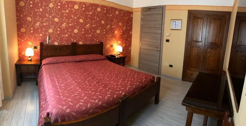 A bedroom with a bed, two bedside tables with lamps, a wooden wardrobe, and a desk.