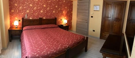 A bedroom with a bed, two bedside tables with lamps, a wooden wardrobe, and a desk.