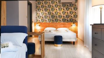 A modern hotel room with a wooden headboard, a bed with white linens, a blue ottoman, a wooden nightstand, and a wall-mounted air conditioner.