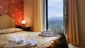 Une chambre d’hôtel avec un lit, une table de chevet, une lampe et une vue sur la mer, visible à travers une grande fenêtre.