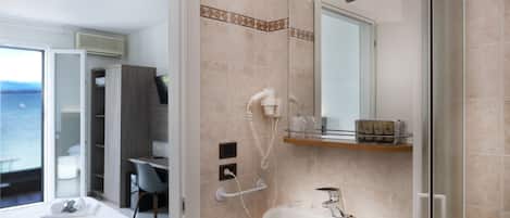 A modern bathroom with a large sink, a mirror, and a shower. There is a desk and chair in the adjacent room.