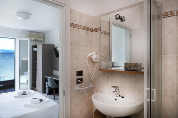 Un baño moderno con un lavamanos grande, un espejo y una ducha. En la habitación contigua hay un escritorio y una silla.