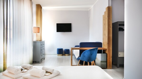 Una habitación de hotel moderna con una cama, un escritorio con una silla, un televisor en la pared y un armario.