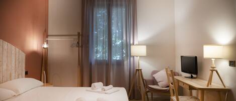 A hotel room with a bed, a desk, a chair, a TV, and a window with curtains.