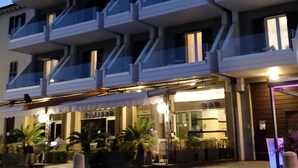 Un hôtel à plusieurs étages, doté de balcons, d’une entrée bien éclairée et d’un espace extérieur aménagé pour s’asseoir.