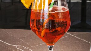 Un verre à cocktail, une tranche d’orange et une paille rayée de vert et de blanc sont posés sur une table.