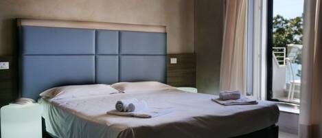 A modern hotel room with a large bed, a bedside table, and a view of the outdoors.