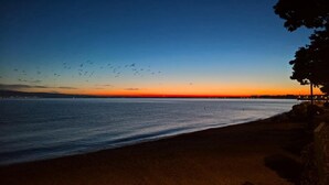 Une plage offrant une vue sur le coucher de soleil, avec des eaux calmes et une côte lointaine illuminée.