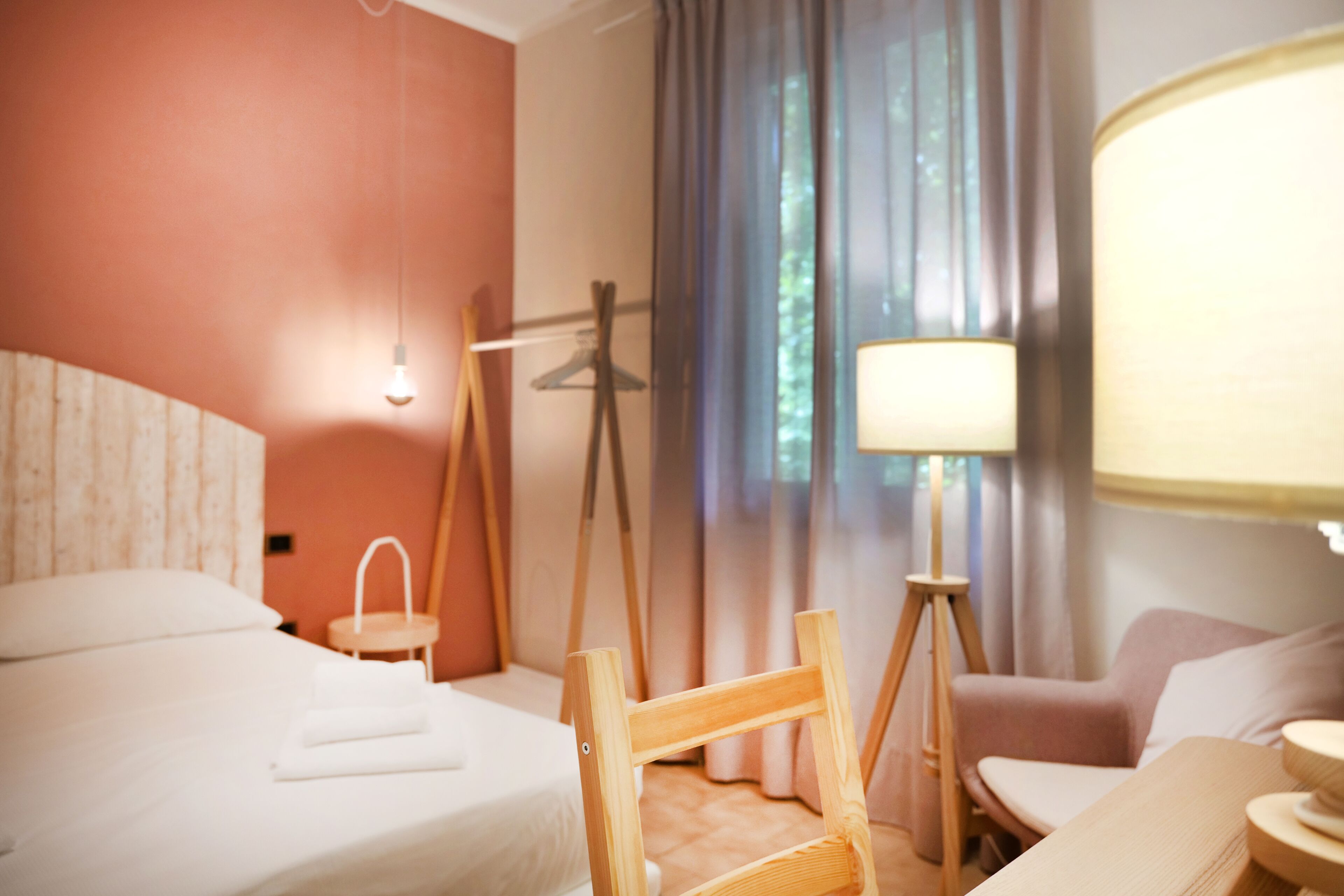 Una habitación de hotel con cama, una silla, una mesa, una lámpara y cortinas.