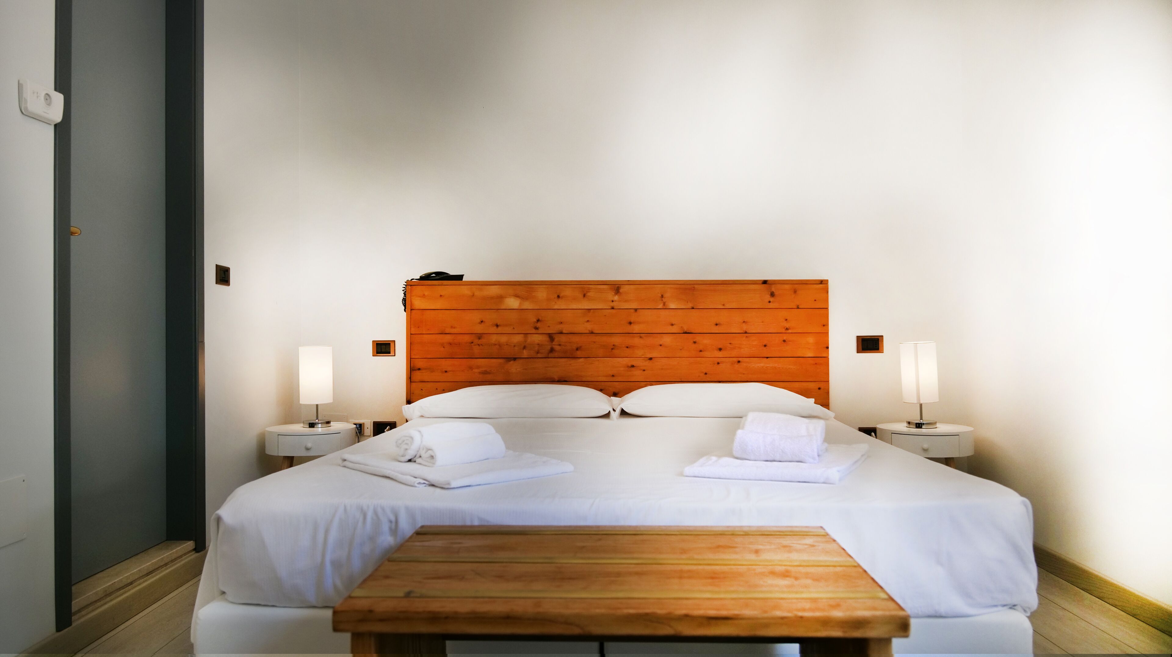 Una cama bien hecha con sábanas blancas, dos mesitas de noche con lámparas y un cabecero de madera.