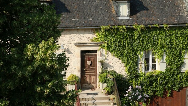 Une maison en pierre avec un toit à forte pente, une porte en bois et une allée gravillonnée.