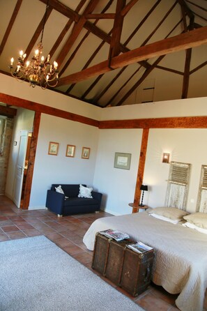 A bedroom with a large bed, a blue sofa, a chandelier, and a suitcase. - Domaine le Muret (Le Bas-Segala)