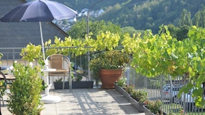 A patio with a table and chairs, a large potted plant, and a grapevine. - Weingut Sauer-Kettermann (Enkirch)