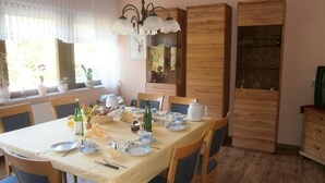 A dining area with a table set for four, surrounded by wooden chairs with blue cushions. There is a chandelier above the table, and a cabinet with glassware to the right. - Weingut Sauer-Kettermann (Enkirch)