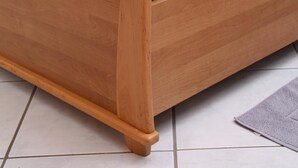 A wooden bed with a white mattress and pillows, a bedside table with a lamp, and a grey rug on a tiled floor. - Weingut Sauer-Kettermann (Enkirch)