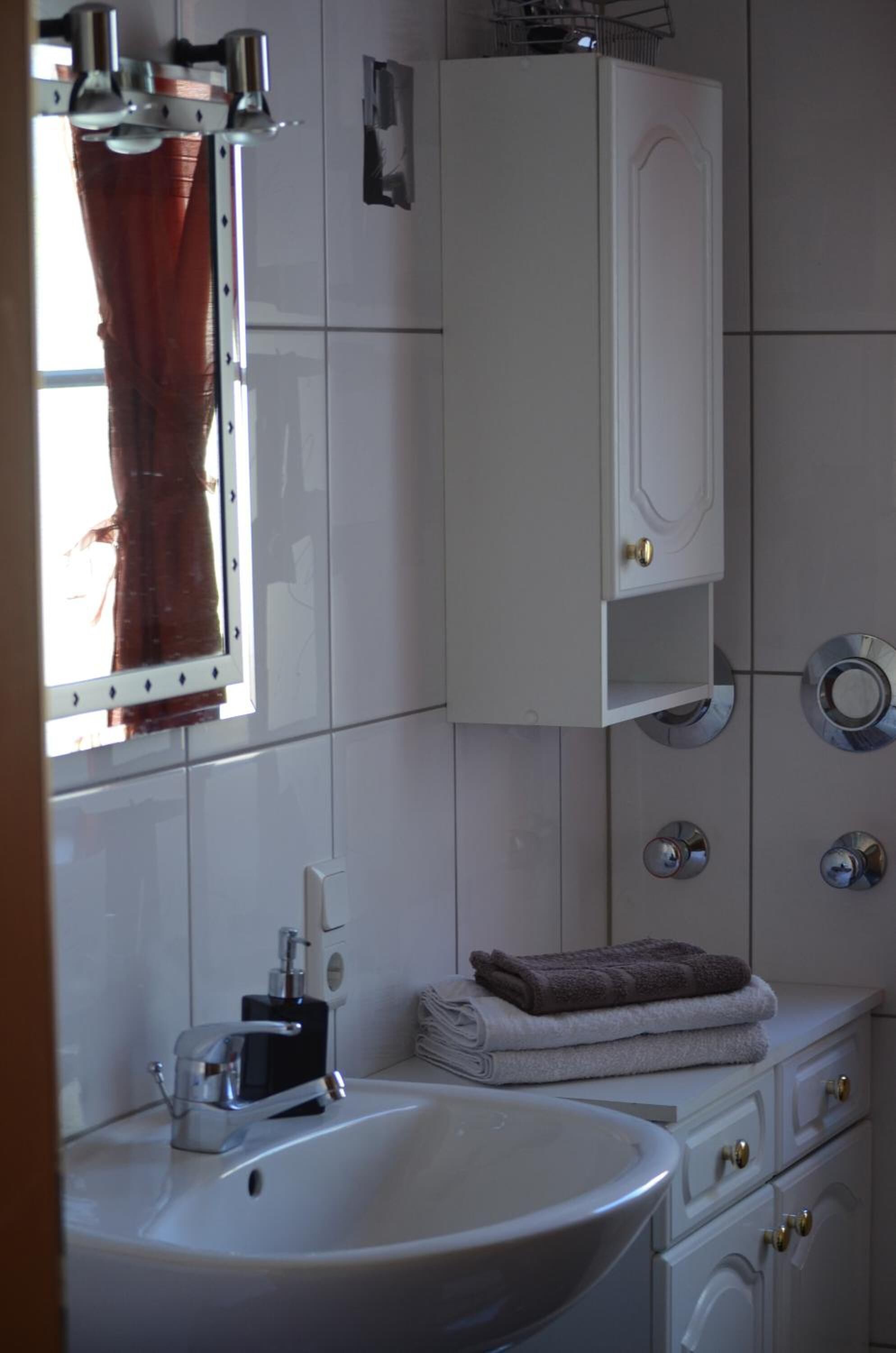 Een badkamer met een witte wastafel, een spiegel, een handdoekhouder en een kastje.