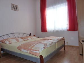 Une chambre à coucher avec un lit, une tête de lit en bois et une fenêtre ornée de rideaux rouges.