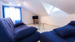 A modern living room with a sloped ceiling, a glass table, and a flat-screen TV.
