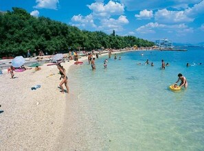 A beach with clear water, people swimming and sunbathing, and a forested area in the background. - Maretsol Vacation House (Sveti Filip i Jakov)