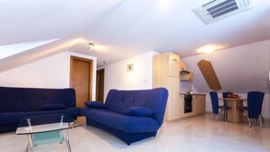 A compact living space with a sofa, a glass-top coffee table, a dining area with a small table and chairs, and a kitchenette.