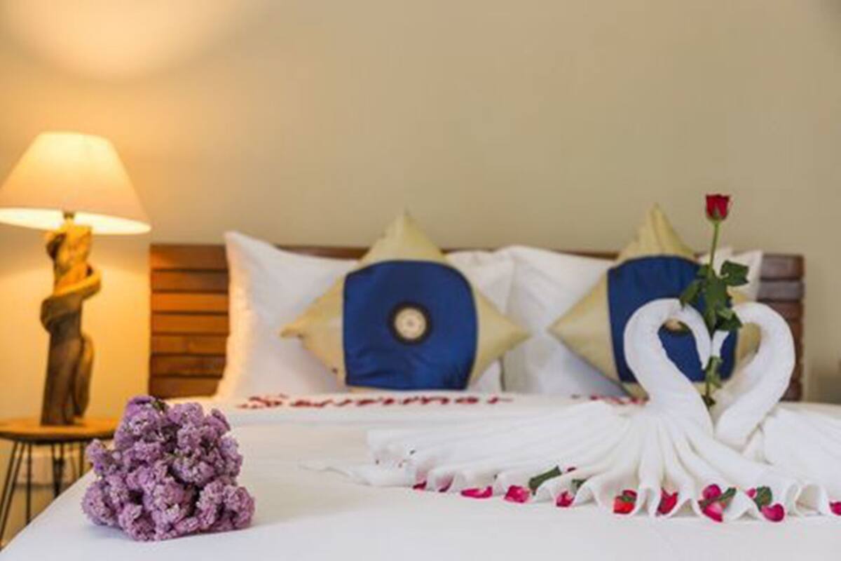 Een netjes opgemaakt bed met witte lakens, een blauw kussen en een decoratieve zwaan van handdoeken.