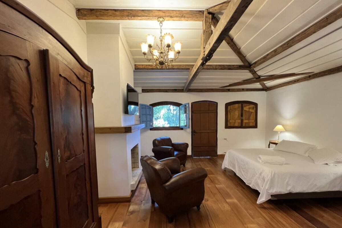 A bedroom with a bed, a fireplace, leather chairs, and wooden floors.