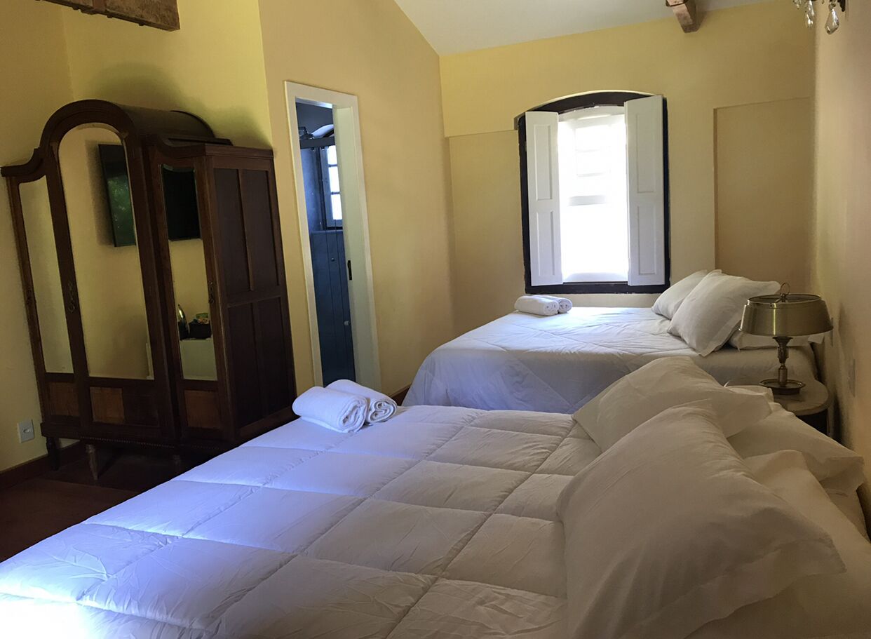 A hotel room with two beds, a wooden wardrobe, a mirror, and a lamp.