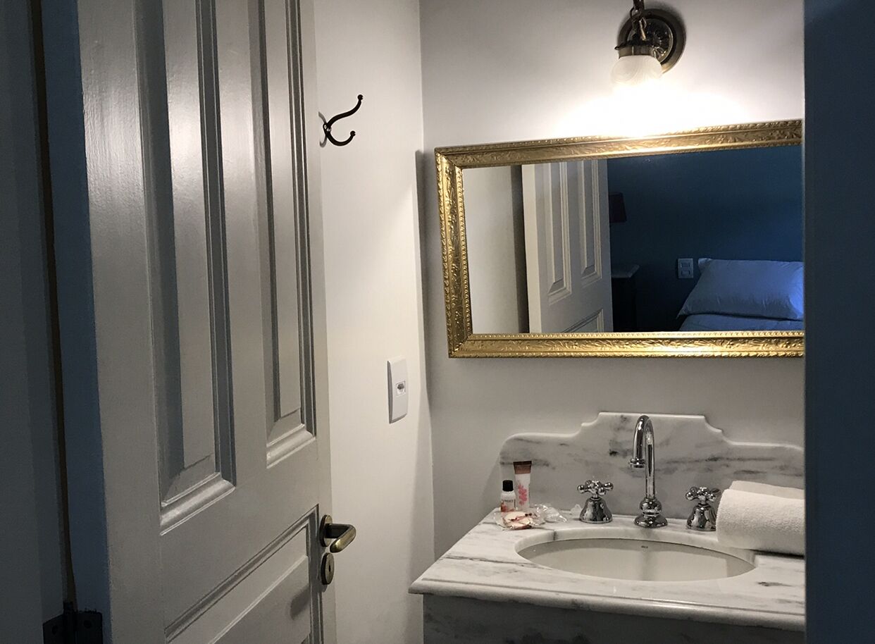 A bathroom with a white sink, a gold-framed mirror, and a door with a simple handle.